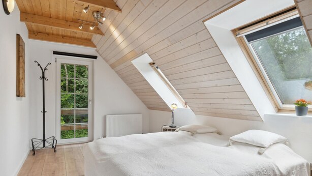 Ein Schlafzimmer mit schrägem Dach, einem Bett, einem Fenster und einer Heizung.