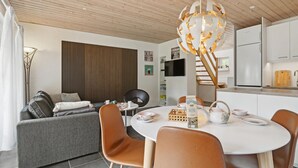Ein modernes Wohnzimmer mit einem runden Esstisch, braunen Ledersesseln, einem grauen Sofa und einer Holzbalkendecke.
