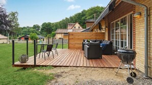 Eine Holzterrasse mit Gartenmöbeln, einem Grill und Blick auf eine Wohngegend.