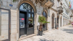 Un bâtiment historique abritant un distributeur automatique de billets noir, un palmier en pot et une enseigne indiquant qu’il s’agit d’un hôtel-boutique.