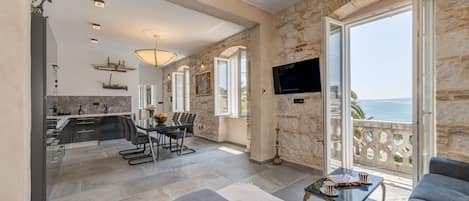 Amplia sala de estar con balcón con vista al mar, cocina moderna y televisor de pantalla plana montado en la pared.