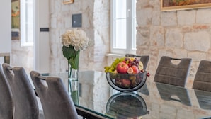 Une table à manger avec un panier de fruits, des chaises et un vase de fleurs.