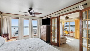 Ein Schlafzimmer mit einem großen Bett, einem Schminktisch, einem Fernseher und Blick auf das Wasser.