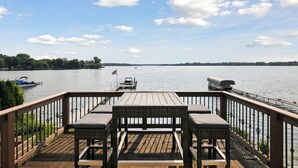 Eine Holzterrasse mit Tisch und Stühlen mit Blick auf einen See und Boote.
