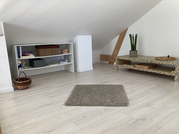 A room with a sloped ceiling, a white bookshelf, a wooden bench, a grey rug, and a potted plant. - Maison Bord de mer Golfe du Morbihan (Vannes)