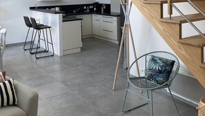 A modern kitchen with a central island, wooden staircase, and a seating area with a chair and sofa. - Maison Bord de mer Golfe du Morbihan (Vannes)