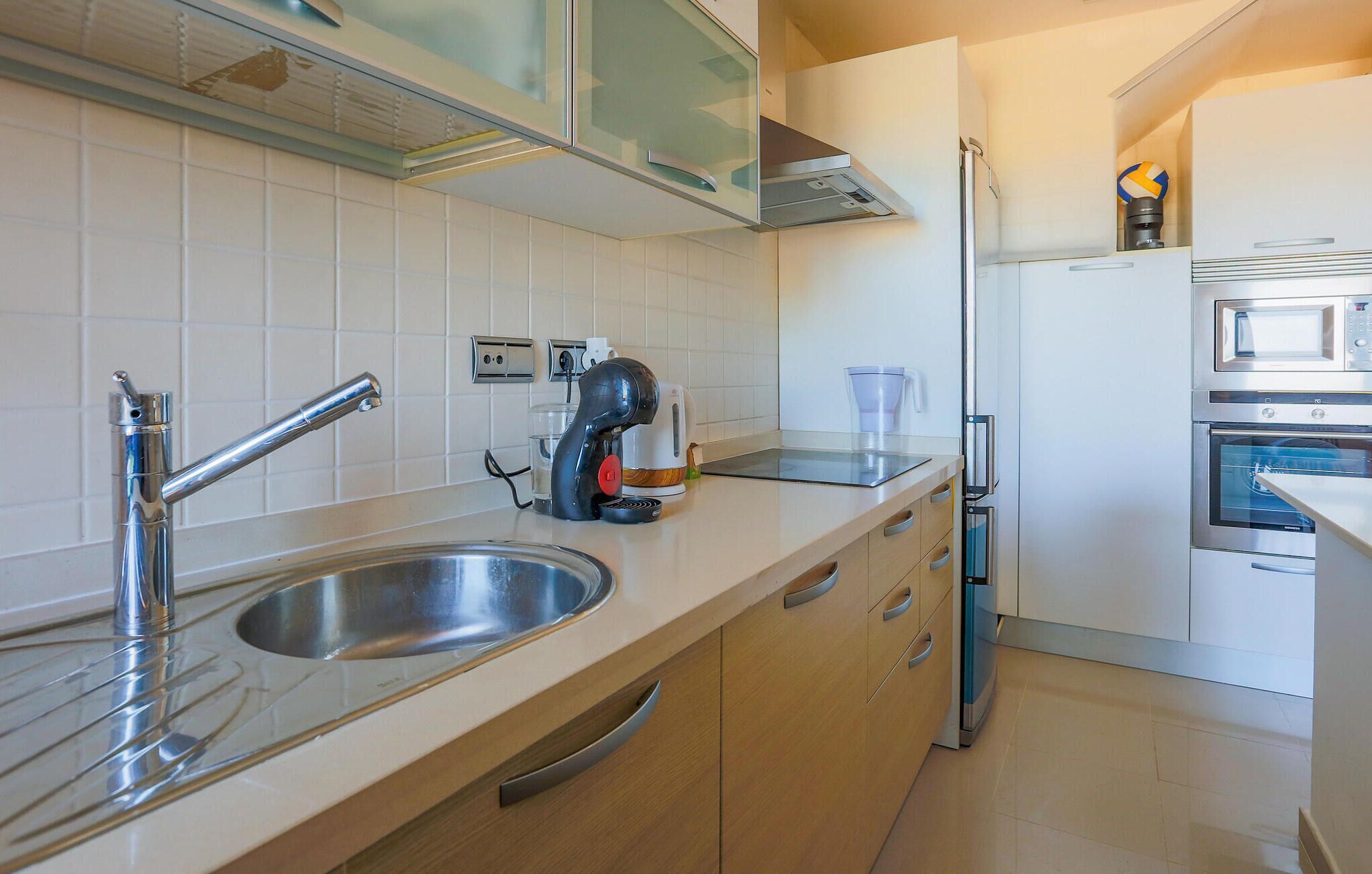 Una cocina moderna con un lavamanos de acero inoxidable, una tetera y un microondas.