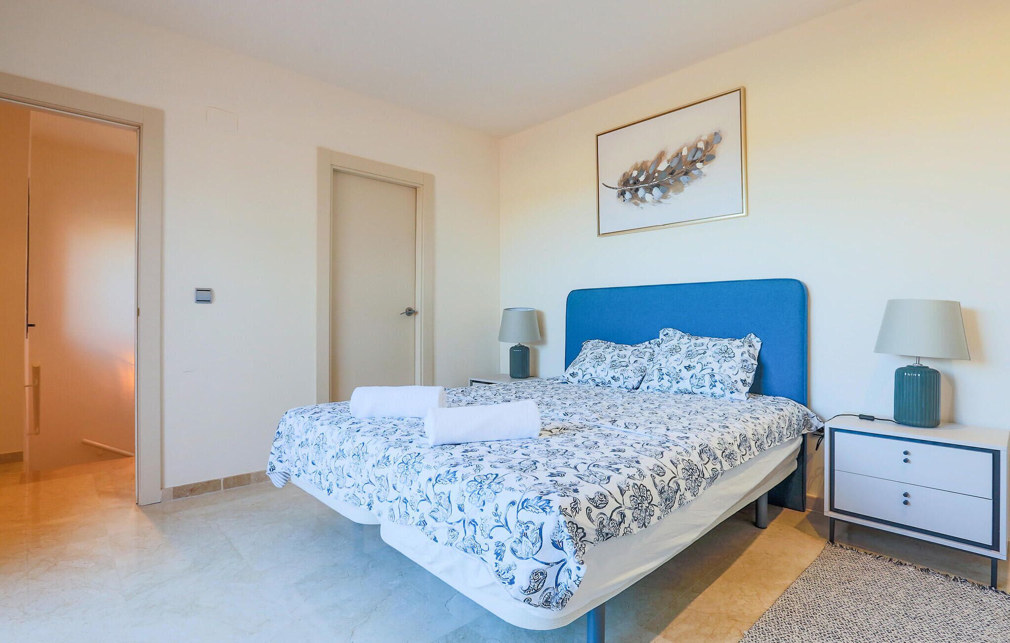 Une chambre à coucher comprenant un lit, des tables de chevet, une commode, une porte et une œuvre d’art accrochée au mur.