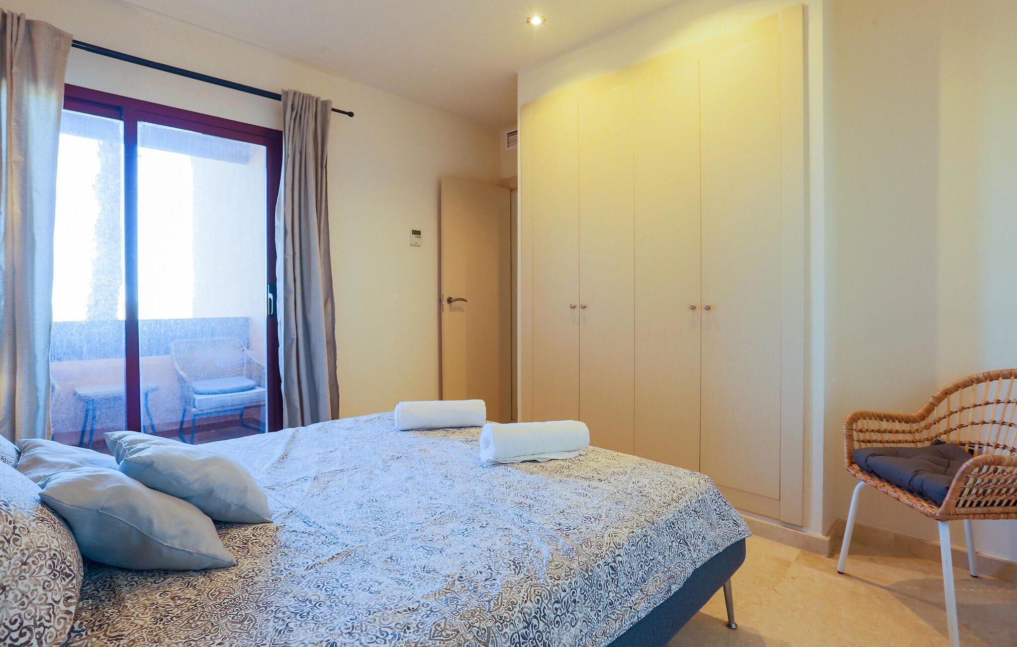 Un dormitorio con una cama grande, una silla, un armario y vistas al exterior.