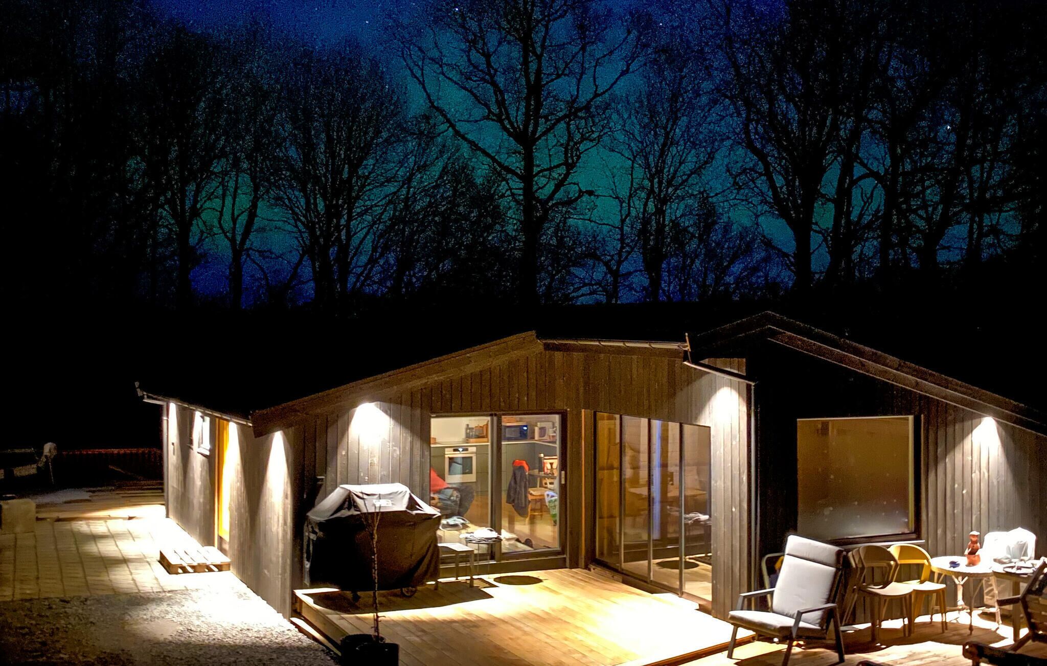Eine Holzhütte mit einer Terrassenfläche, einem Grill und einem Esstisch mit Stühlen.