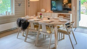 A dining area with a wooden table set for four, a television mounted on the wall, and a window with a view of greenery outside. - Gorgeous home in Skjold (Skjold)