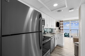 Une cuisine moderne dotée d’appareils électroménagers en acier inoxydable, de meubles blancs et offrant une vue sur l’océan.