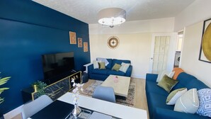 Ein Wohnzimmer mit Fernseher, blauen Sofas, einem Couchtisch und einer Deckenleuchte.