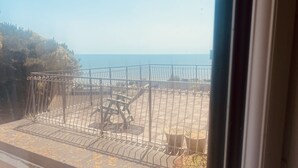 Blick durch ein Fenster auf einen Balkon mit Metallgeländer, einem kleinen Tisch und Topfpflanzen.