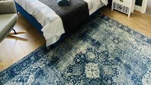 Ein modernes Schlafzimmer mit einem großen Bett, einer blauen Kopfteil, einem gemusterten Teppich und einem Stadtbild an der Wand.