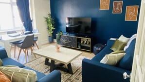 Ein Wohnzimmer mit blauen Sofas, einem Esstisch und einem Fernseher.