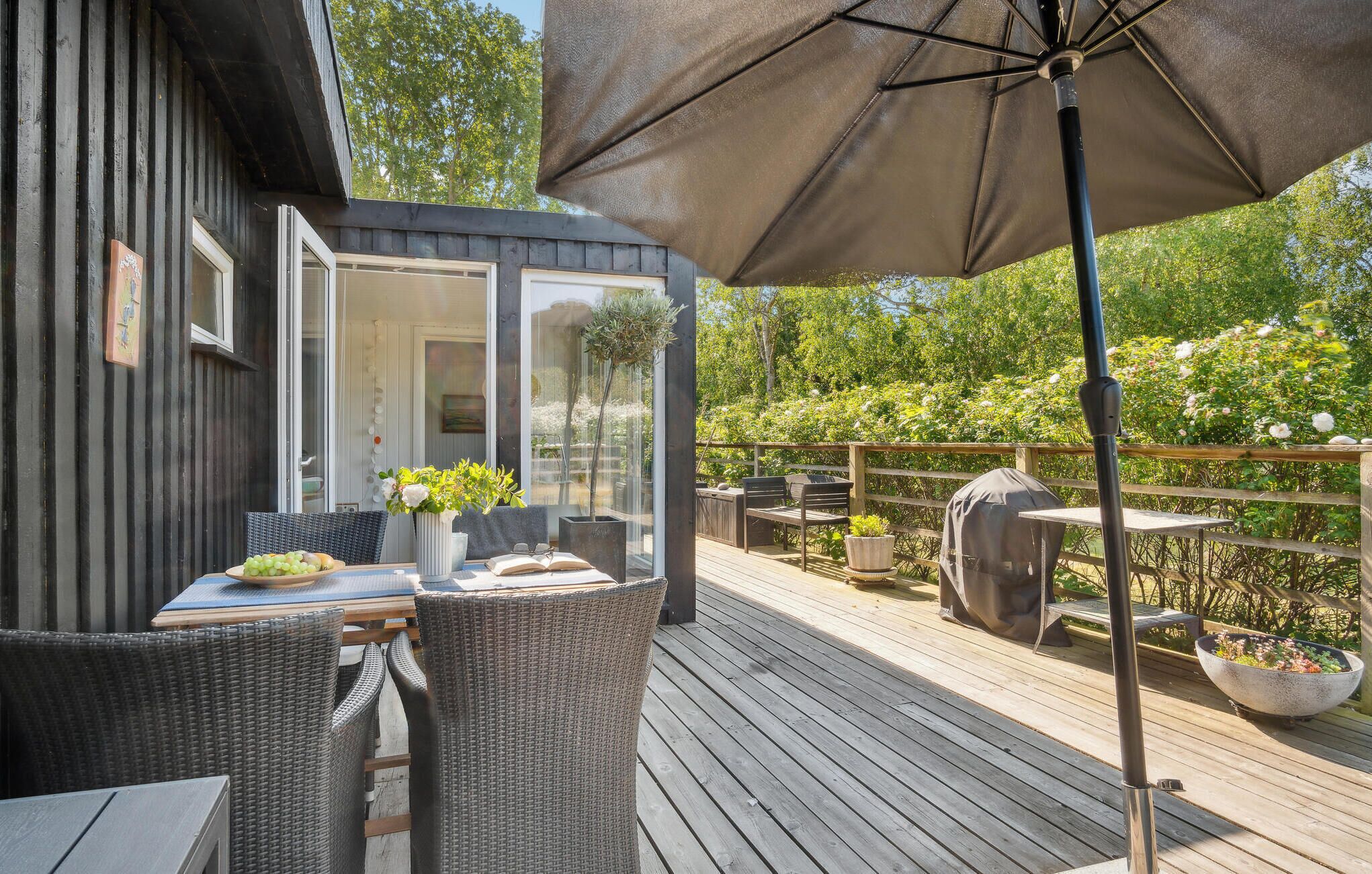 Un patio al aire libre con mobiliario de mimbre, una mesa con un jarrón de flores y una parrilla.