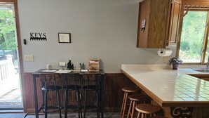 A kitchen with a wooden island, bar stools, a wooden cabinet, and a window with a view of greenery.