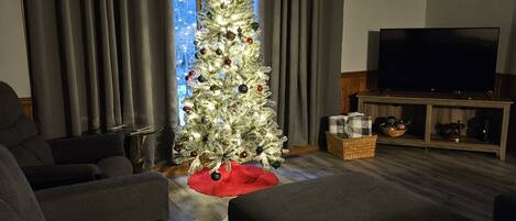 A living room with a white Christmas tree, grey curtains, a flat-screen TV, and a wooden coffee table.