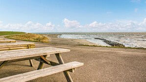 A picnic table on a gravel path with a view of the ocean and a grassy hill in the background. - Nice home in Heinkenszand with WiFi (Heinkenszand)