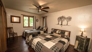 A bedroom with two beds, a ceiling fan, a chair, a window, and a wall-mounted lamp. - Whispering Pines By The Bay, quiet seclusion near water and town (Sturgeon Bay)