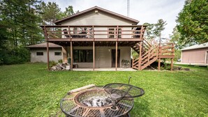 A two-story house with a covered patio and a fire pit in the front yard. - Whispering Pines By The Bay, quiet seclusion near water and town (Sturgeon Bay)