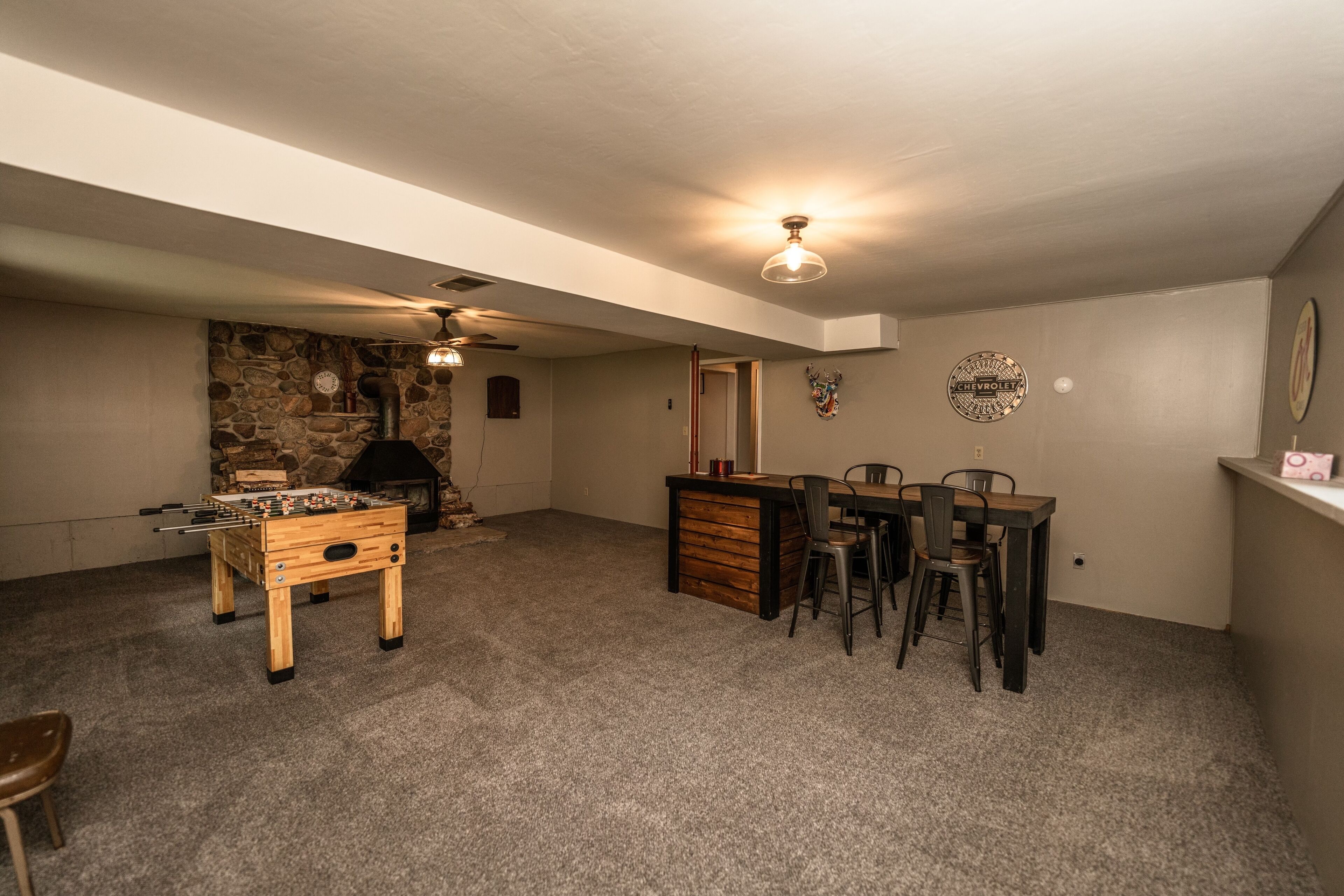 A cozy room with a foosball table, a fireplace, a dining area with chairs, and a ceiling fan.