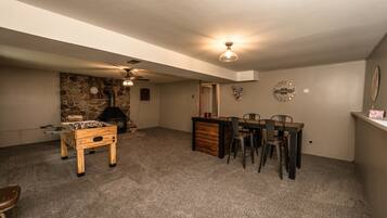 A cozy room with a foosball table, a fireplace, a dining area with chairs, and a ceiling fan.