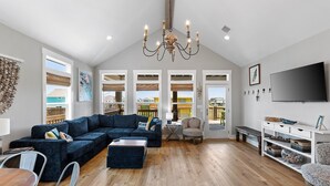 A spacious living room with a large sectional sofa, a coffee table, and a TV on a white console. - Steps from Beach: Sleeps 15, Hot Tub, Pet-Friendly (Crystal Beach)