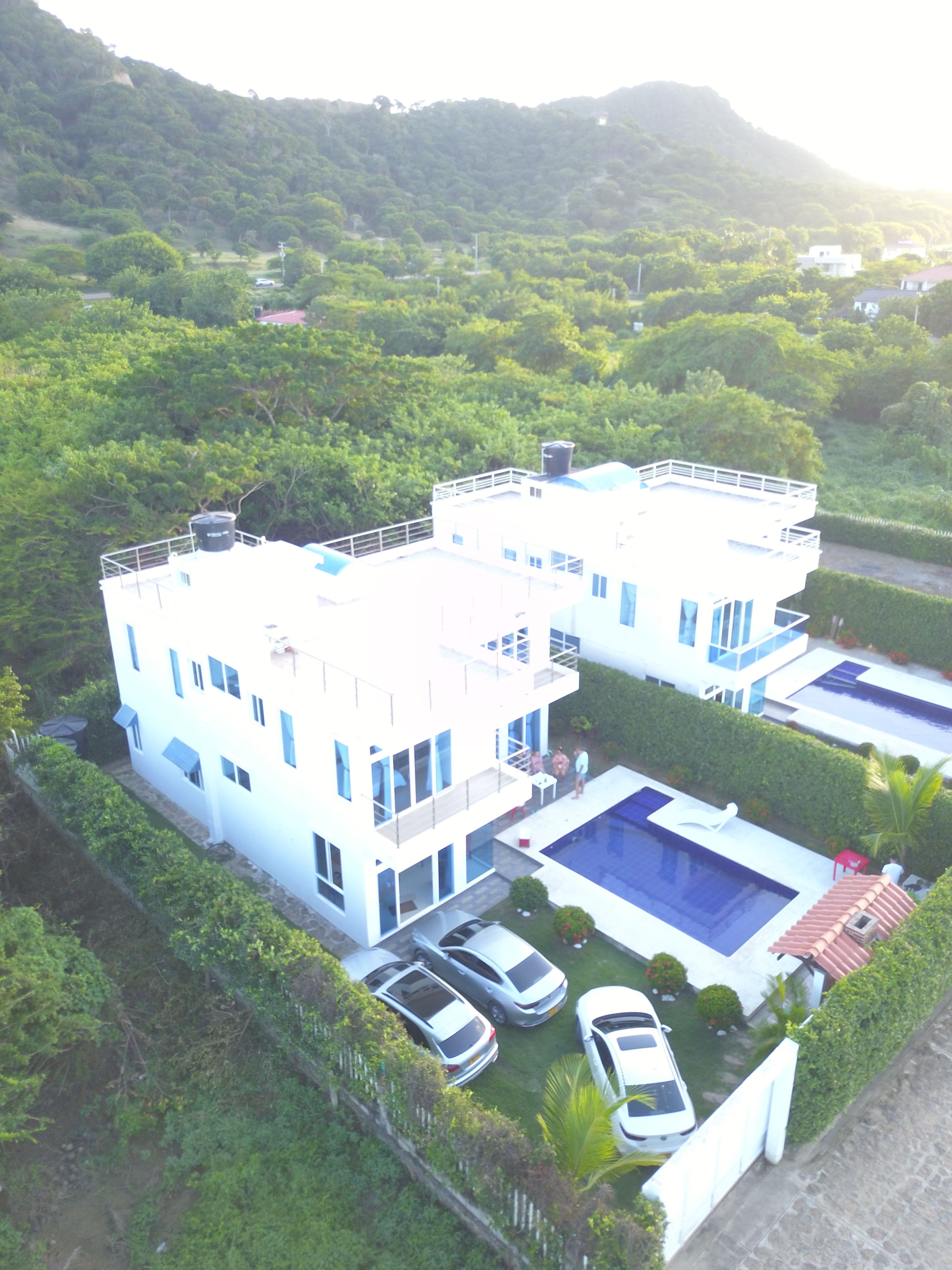 Une maison moderne à deux étages, dotée d’une piscine, entourée d’une végétation luxuriante et de collines.