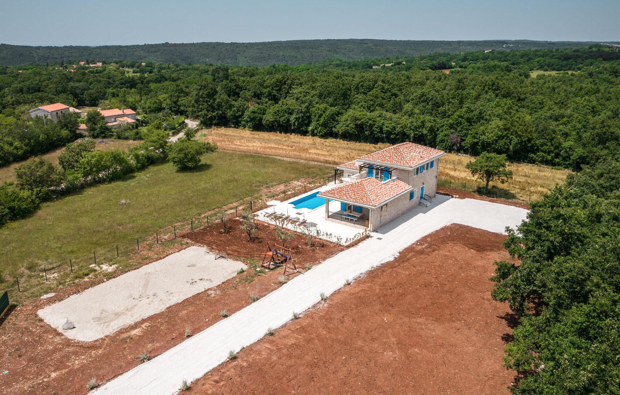 A modern two-story house with a swimming pool, surrounded by a large garden and a forested area.