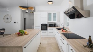A modern kitchen with white cabinetry, a black induction cooktop, and a wooden countertop. - Stunning home in Pifari (Pifari)