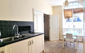 Compact kitchen with a modern design, featuring a tiled backsplash and stainless steel sink, adjacent to a dining area with a table and chairs near a window with an outside view.