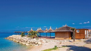 A beachside property with thatched umbrellas, a wooden building, and a rocky shoreline.