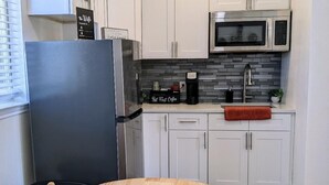 Una cuina moderna amb armaris blancs, un frigorífic d'acer inoxidable, un microones i una cafetera.