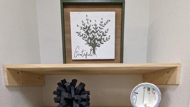 Una estant amb una obra d'art emmarcada, un objecte decoratiu, un mirall, i tovalloles i productes de tocador ordenats.