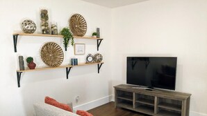 Un saló amb un sofà gris, prestatges de fusta amb objectes decoratius, un televisor sobre un suport de fusta i un paviment de fusta.