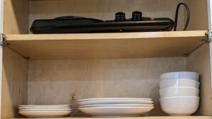 Un armari de fusta amb calaixos que contenen plats, bols, gots i un objecte negre.