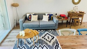 Ein Wohnzimmer mit grauem Sofa, einem gemusterten Teppich, einem Holztisch und einem Schreibtisch mit Spiegel.