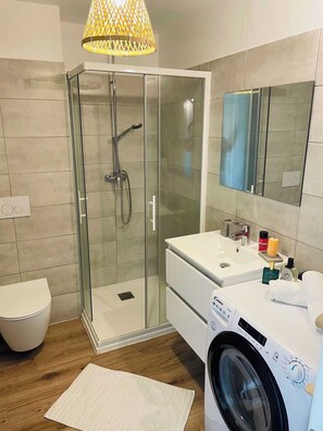 Ein modernes Badezimmer mit Glasdusche, integriertem Waschbecken, Toilette und Waschmaschine.