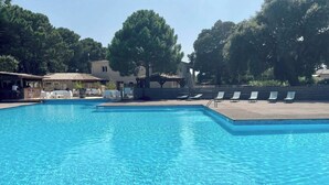 Ein klares, blaues Schwimmbecken mit Liegestühlen und einem überdachten Bereich mit Tischen und Stühlen.