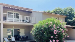 Ein zweistöckiges Gebäude mit Balkon, Sitzgelegenheit im Freien und einem großen, blühenden Busch.