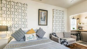 A modern bedroom with a large bed, a sofa, and a small kitchen area. - Spanish Colonial Revival Studio Unit 3 (Phoenix)