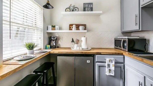 A compact kitchen with a refrigerator, microwave, and a wooden countertop. There are two bar stools and a shelf with kitchen items. - Spanish Colonial Revival Studio Unit 3 (Phoenix)