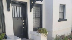 A modern house with a black door, white exterior, and a small porch with steps leading to the entrance. - Spanish Colonial Revival Studio Unit 3 (Phoenix)