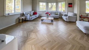 A spacious living room with a herringbone floor, multiple seating areas including sofas and armchairs, and large windows providing natural light. - 2 bedroom cozy home in Traryd (Traryd)