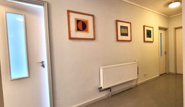 Un couloir avec trois œuvres d’art encadrées accrochées au mur, un radiateur et une porte sur la gauche.