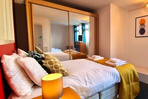 Une chambre d’hôtel avec deux lits, un grand miroir, une table de chevet et une œuvre d’art accrochée au mur.