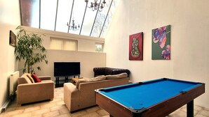 Un salón con mesa de billar, sofás, televisor y obras de arte en las paredes.