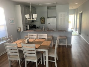 Una cocina moderna con armarios blancos, una isla central y un comedor con mesas y sillas de madera.